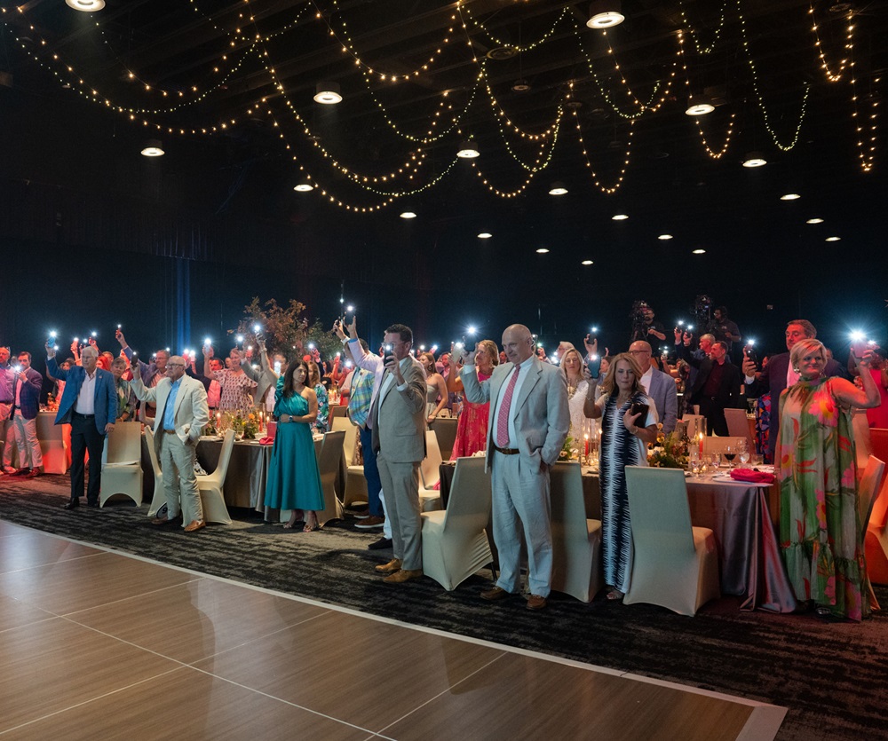 Crowded ballroom with many people holding up cell phones with the flashlight function turned on.